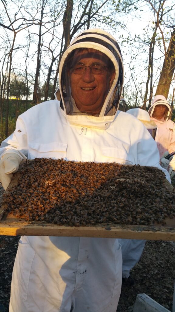 Bee Photo, 2016 Mike Hursey in a beekeeper outfit holding a tray of honey and bees.