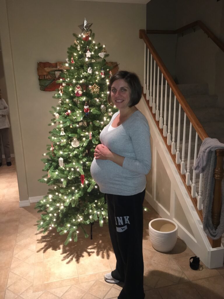 Nadine Long standing in front of a Christmas tree while pregnant.
